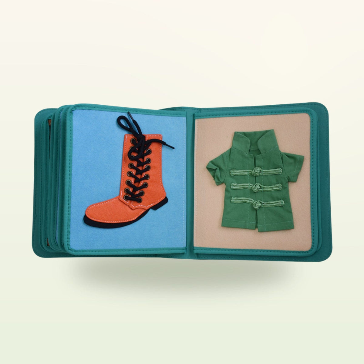 Dressing book fabric page with orange lace-up boot and green jacket with toggle buttons on a soft cream background – from 3 years
