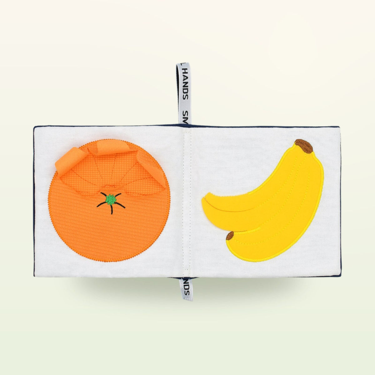 Small Hands Exotic Fruits Montessori cloth book open – orange and banana on a soft cream background – from 0 months
