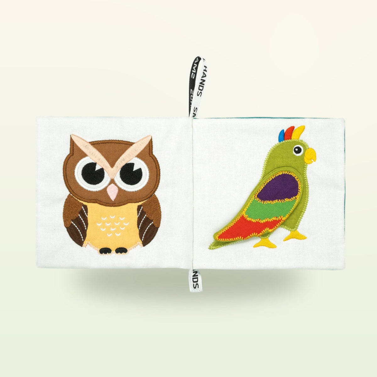 Small Hands Birds Montessori cloth book open – brown owl and colorful parrot on a soft cream background – from 0 months