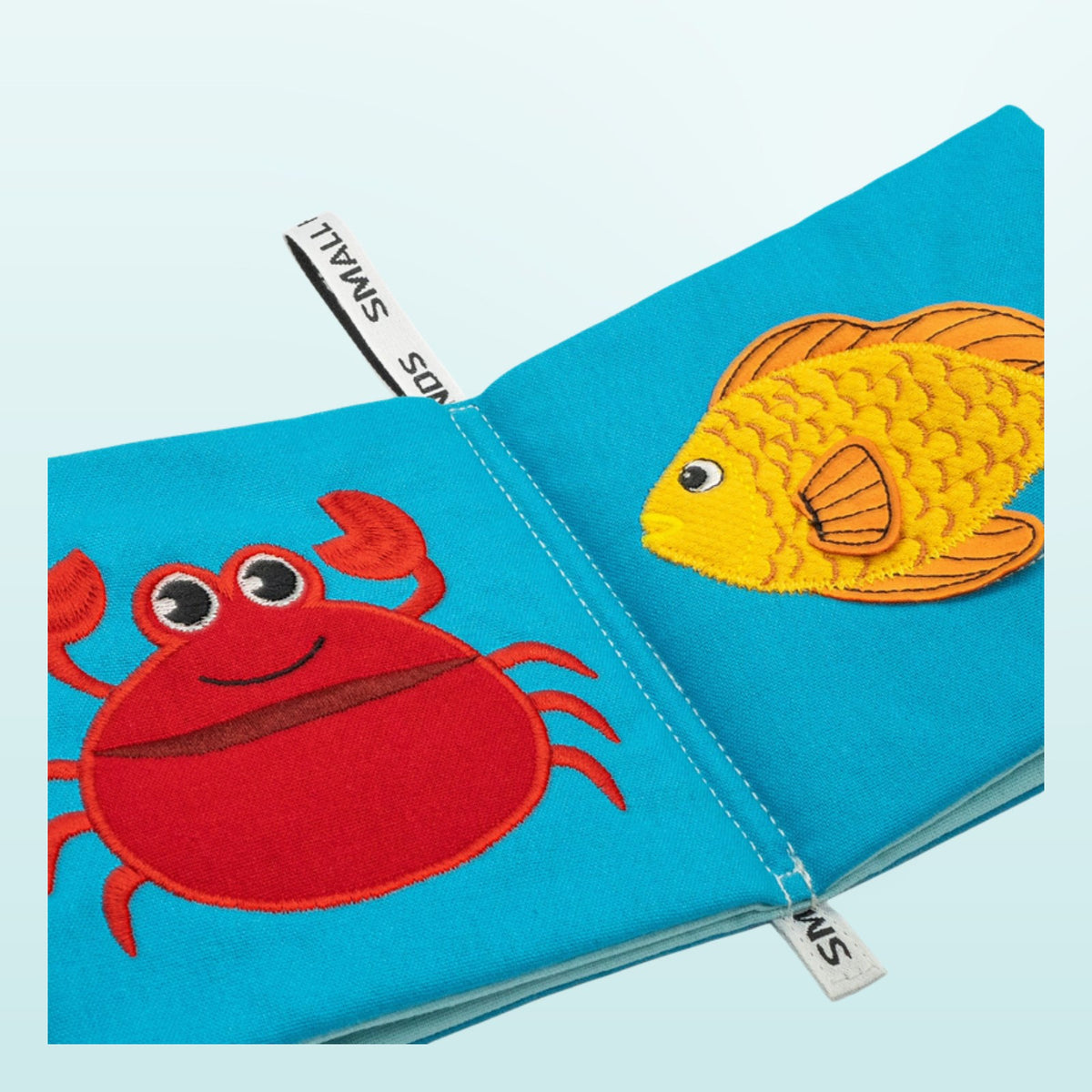 Small Hands Sea Animals Montessori cloth book close-up with crab and goldfish on a soft underwater blue background – from 1 year