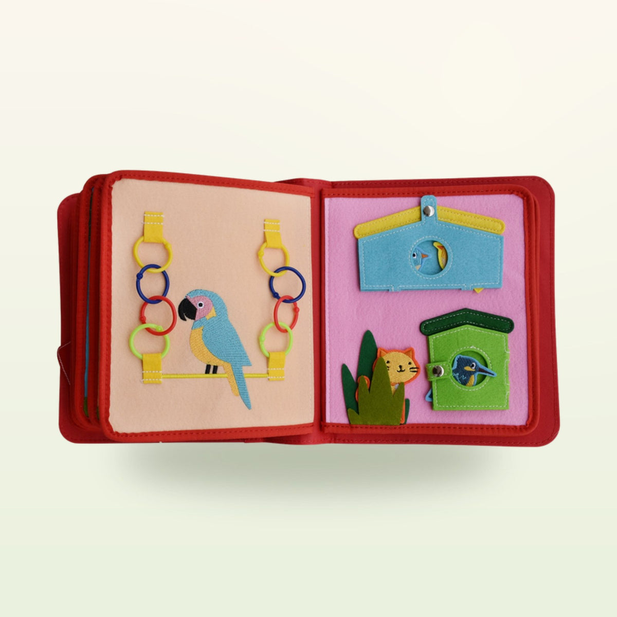 Circus Adventure quiet book bird double page with parrot with felt rings to thread and birdhouse with snap-button flaps on a soft cream background – from 3 years