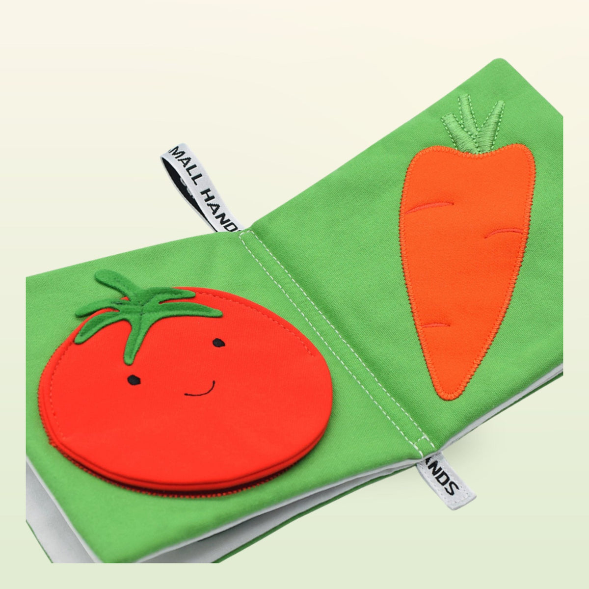 Small Hands Vegetables Montessori cloth book close-up with tomato and carrot on a soft meadow green background – from 1 year