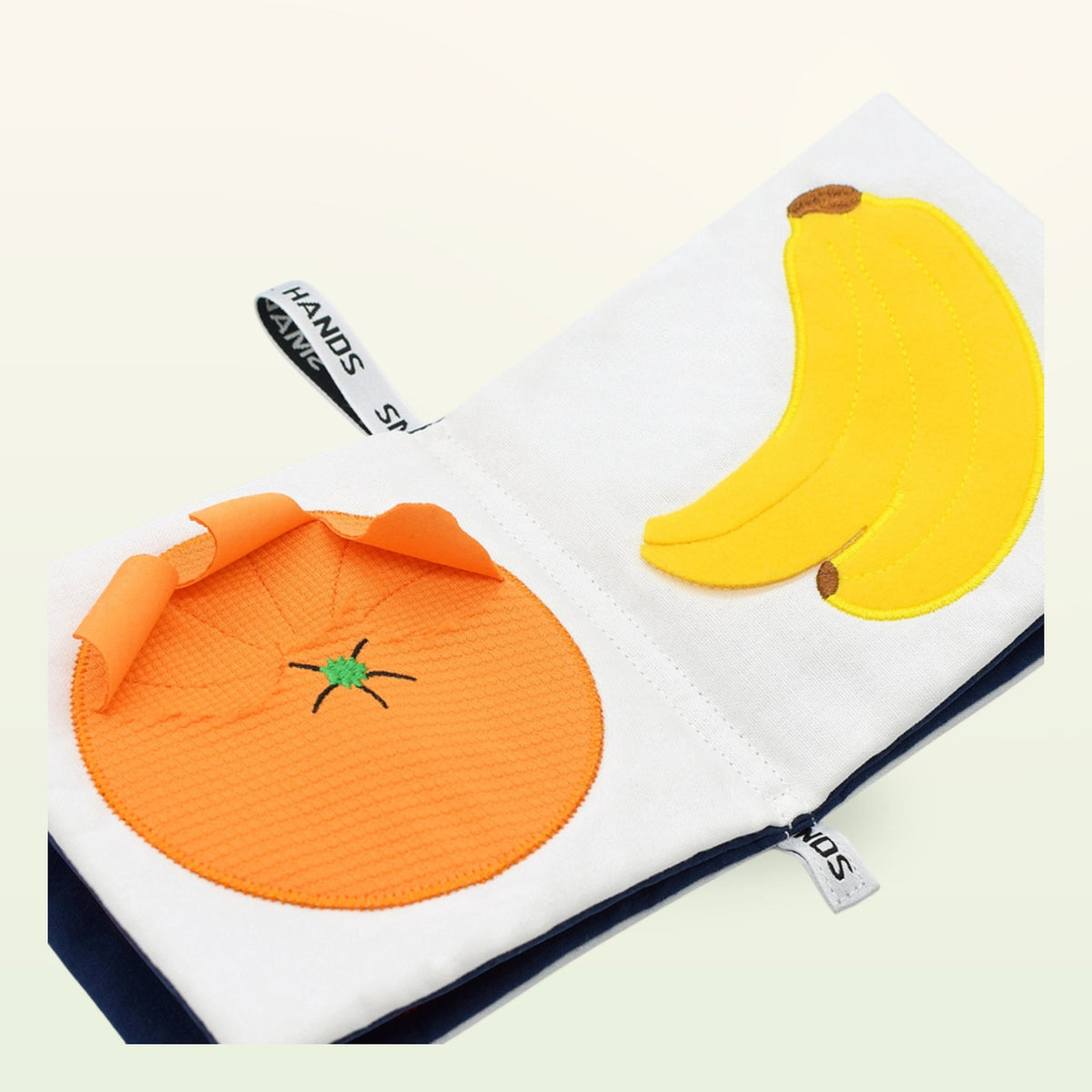 Small Hands Exotic Fruits Montessori cloth book open – orange and banana at an angle on a soft cream background – from 0 months