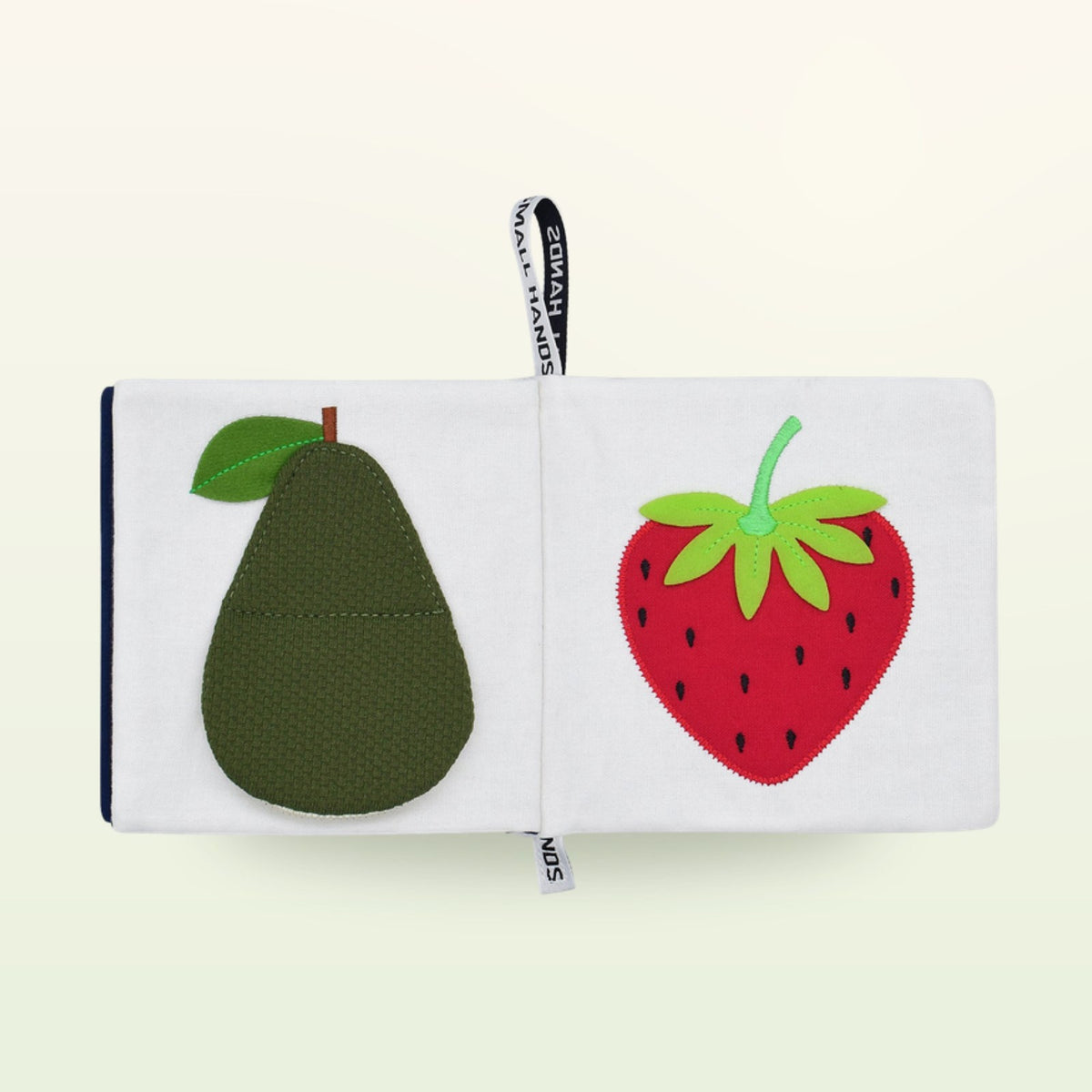 Small Hands Colorful Fruits Montessori cloth book open – green avocado and red strawberry on a soft cream background – from 0 months