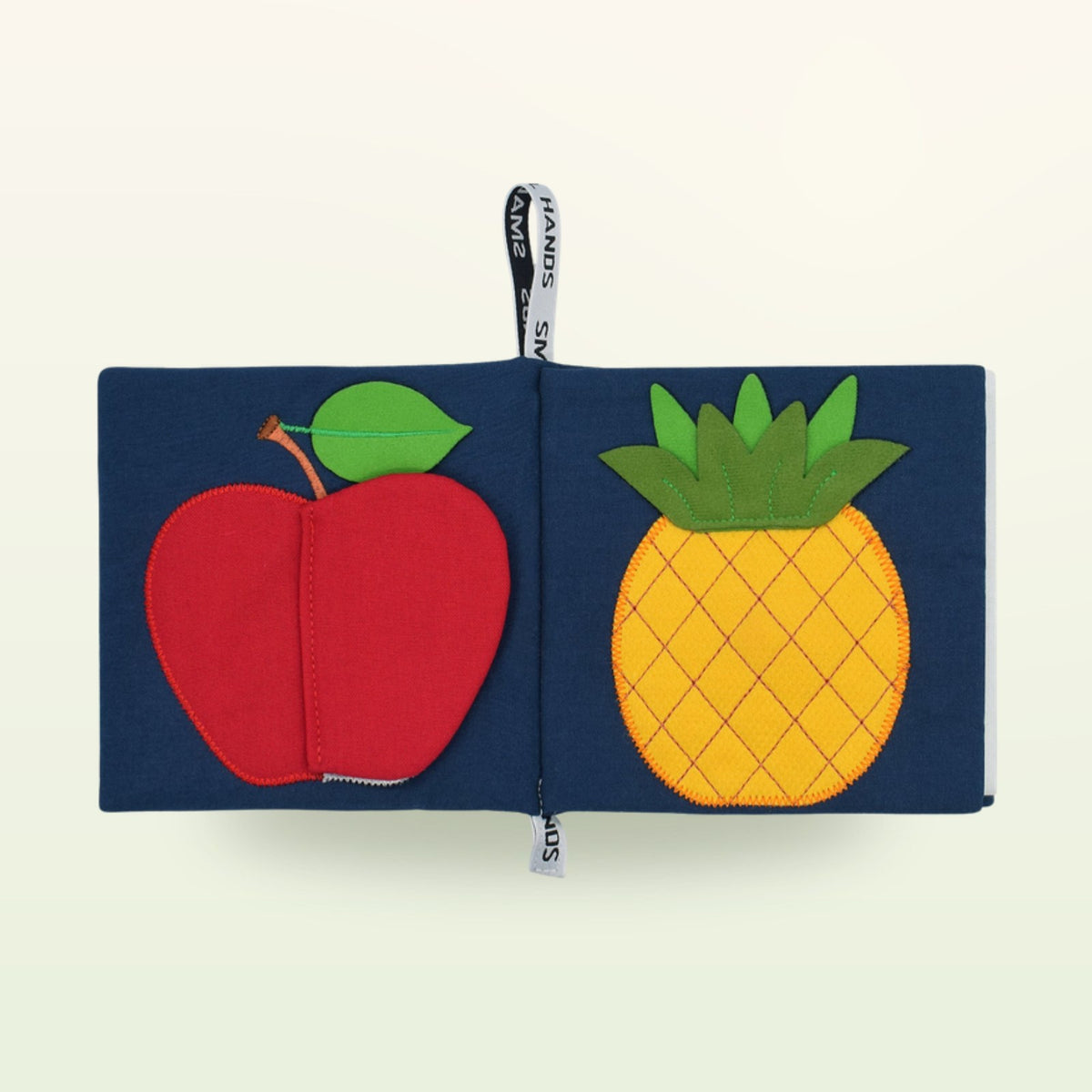 Small Hands Exotic Fruits Montessori cloth book open – apple and pineapple on a soft cream background – from 0 months
