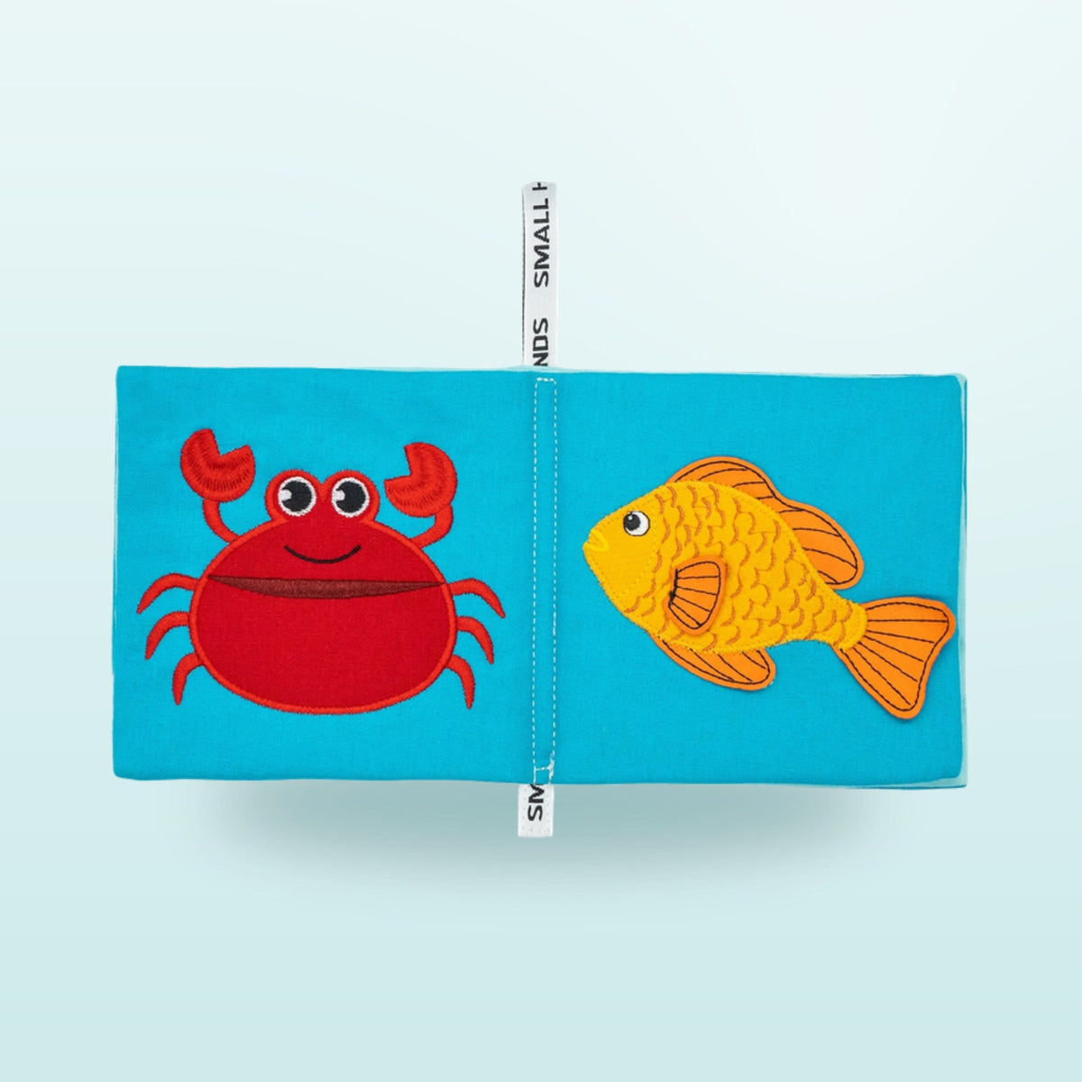 Small Hands Sea Animals Montessori cloth book double page with crab and goldfish on a soft underwater blue background – from 1 year