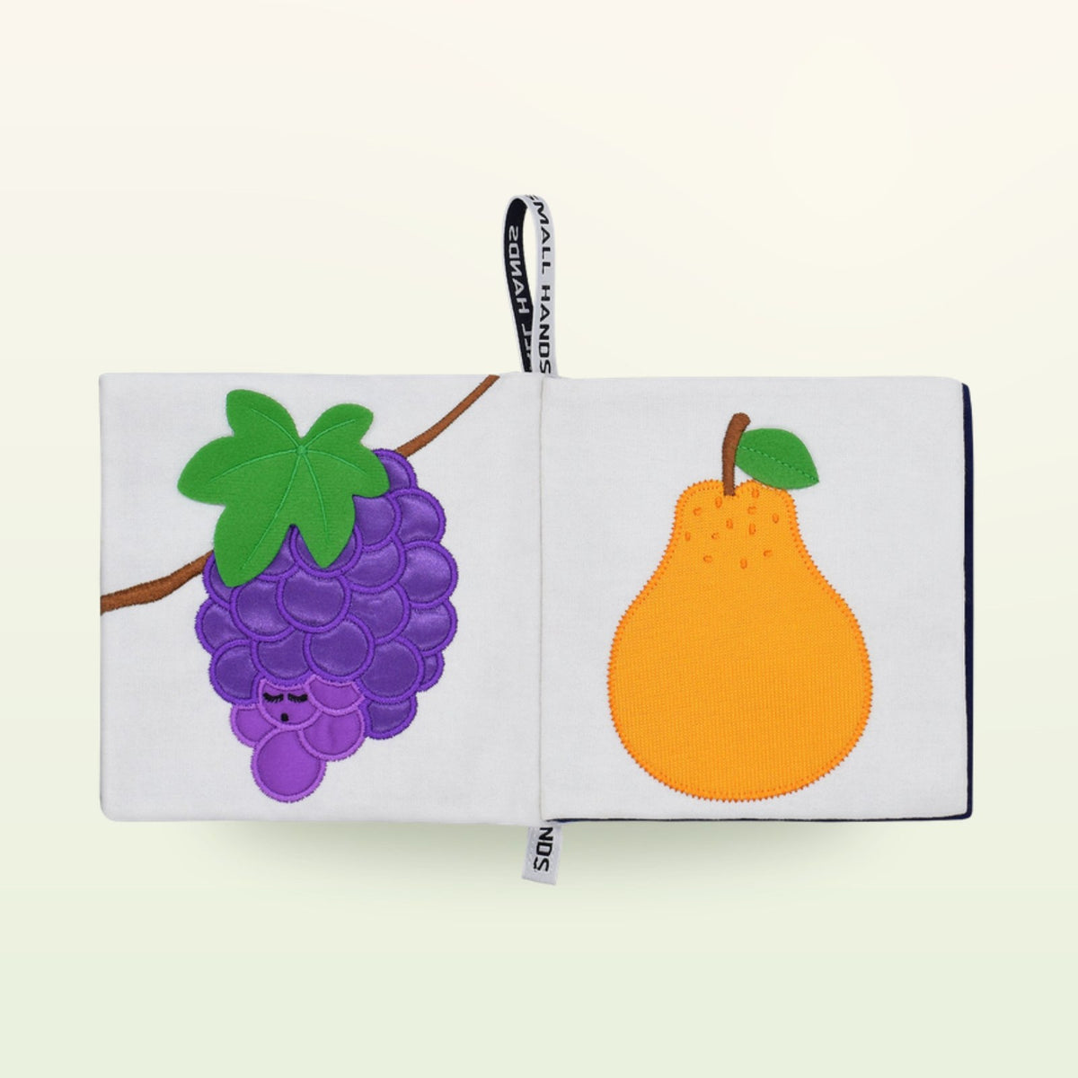 Small Hands Colorful Fruits Montessori cloth book open – purple grapes and orange pear on a soft cream background – from 0 months