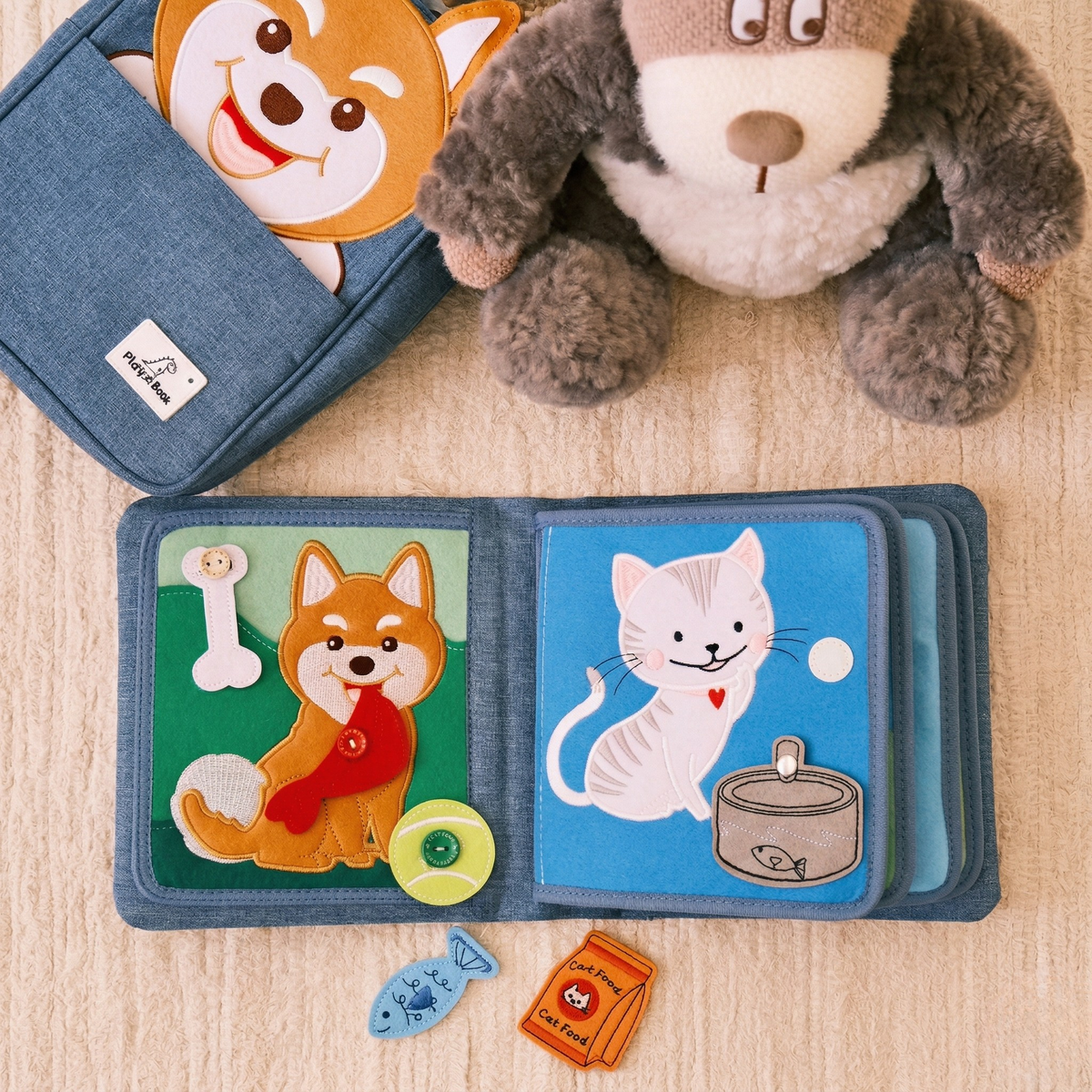Open Pet Friends quiet book: on the left a dog with bone, red buttoned neckerchief and tennis ball; on the right a cat with bowl and fish; in the background a plush dog and Shiba backpack, loose felt pieces in front. From 1 year.
