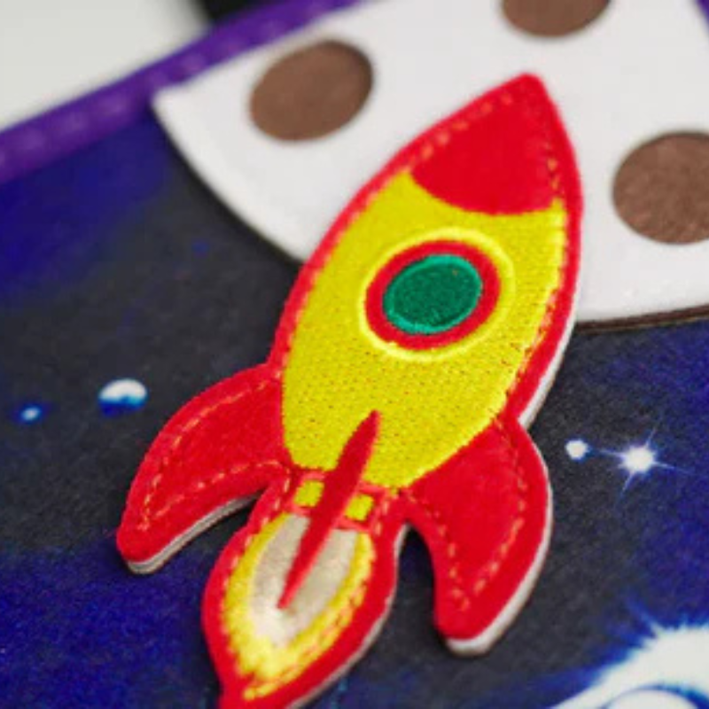 Close-up of the red felt rocket with green porthole on a starry sky in the space quiet book – high-quality craftsmanship
